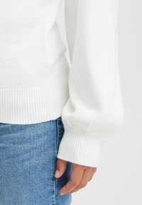 Weißer Strickpullover mit gerippten Bündchen, lockerer Passform und weichem Material, kombiniert mit hellblauen Denim-Jeans.