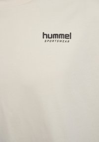 Crème-kleurig T-shirt van katoen, met een zwart "hummel" logo en de tekst "SPORTSWEAR" op de voorkant. Korte mouwen, ronde halslijn.
