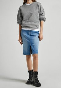 Sudadera gris con acentos de tachuelas, llevada sobre una camiseta blanca. Combinada con una falda de mezclilla azul clara con una abertura frontal y botas de combate negras.
