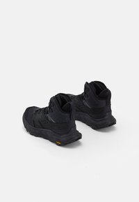 Scarpe da trekking nere con tomaia in mesh testurizzato e sintetico, caratterizzate da un design a caviglia alta e suola Vibram con accenti arancioni.