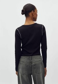 Top negru cu mânecă lungă, cu o textură ribbed, având studuri argintii pe umeri. Asortat cu blugi din denim deschis, cu talie înaltă.