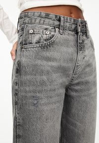 Harmaat farkut, joissa on löysä istuvuus, viisipokkainen malli ja hienovarainen haalistunut rakenne hopeisilla metalliosilla ja napin suljenta.