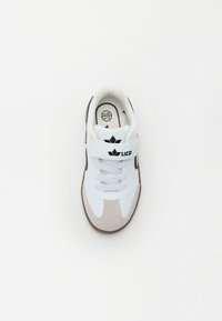 Biele športové topánky s šedými semišovými akcentmi, čiernym brandingom, šnurovaním a pásikom na suchý zips. Gumová podrážka a polstrovaný golier.