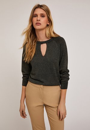 Pulover tricotat gri închis cu un guler rotund și o decupare în formă de cheie. Are mâneci lungi și o textură moale. Este asortat cu pantaloni bej ajustați.