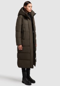 Garšs, olīvu zaļš pufīgs mētelis ar augstu apkakli, ar horizontālu kviltingu, ar rāvējslēdzēja kabatām un melniem akcentiem. Nēsāts ar melnām zābakiem.