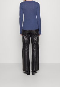 Modrý žebrovaný dlouhý rukáv spárovaný s černými širokými koženými kalhotami. Hladká textura a přiléhavý design doplňují siluetu outfitu.