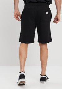 Pantalones cortos negros de algodón con cintura elástica, bolsillos laterales y un bolsillo trasero con una etiqueta. La tela es suave y elástica.