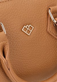 Brun lædertaske med struktureret overflade, der har sølvfarvet hardware og geometrisk logo detalje. Tasken har korte håndtag og synlige stikninger.