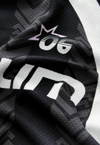 Svart och vit texturerad tyg med stiliserad vit text och en liten rosa stjärna med två djärva, konturerade ögon ovanför.