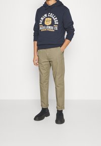 Granatowa bluza z kapturem z żółtym nadrukiem, w połączeniu z jasnooliwkowymi zwężanymi spodniami oraz czarnymi botkami z chropowatą podeszwą.