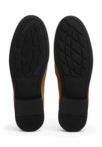 Brown suede shoes with black rubber soles, featuring a textured grip pattern. The soles are flat and designed for comfort and traction.