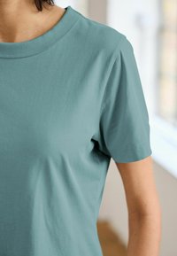 Camiseta de algodón en teal claro con cuello redondo y mangas cortas. Textura suave y costuras mínimas para un aspecto limpio.