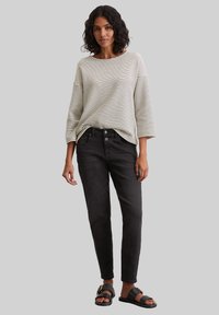Striped long-sleeve top in cream and black, paired with black fitted jeans and black sandals; features relaxed fit and cuffed sleeves.
