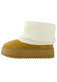 Botte en daim beige avec un col en maille côtelée blanche épaisse, dotée d'une semelle épaisse beige avec une adhérence texturée et d'un design à bout arrondi.