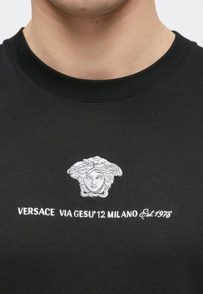 Μαύρο βαμβακερό μπλουζάκι με λευκό κεντητό λογότυπο Μέδουσας και το κείμεν�ο "VERSACE VIA GESU'12 MILANO Est. 1978" από κάτω. Στρογγυλή λαιμόκοψη.