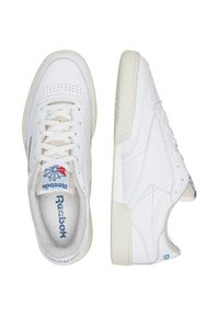 Bílé kožené tenisky s perforovanou špičkou, plochými tkaničkami a logem Reebok na jazyku. Obsahují texturovanou gumovou podrážku a modré akcenty.