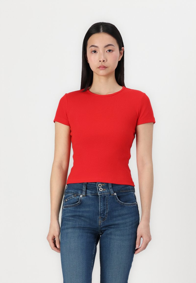 T-shirt rouge ajusté à manches courtes et col rond, en tissu côtelé, associé à un jean bleu taille haute. Texture lisse.