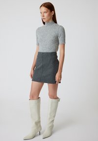 Grijze gebreide trui met korte mouwen, gecombineerd met een grijze mini-jurk en strakke witte laarzen tot de knie. Eenvoudig, schoon ontwerp en texturen.