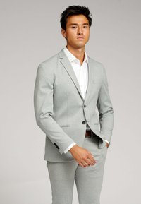 Lys grå jakkesæt lavet af glat stof, der har en enkeltrækket jakke med en notch-lapel og matchende bukser, stylet med en hvid skjorte.
