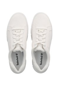 White canvas sneakers with flat laces, padded collar, and textured surface, featuring a blue inner lining and Timberland logo inside.
