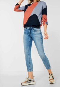 Färgblockerad sweatshirt i röd, marinblå och ljusgrå; åtsittande ljusblå jeans; avslappnade sneakers med flerfärgade detaljer.