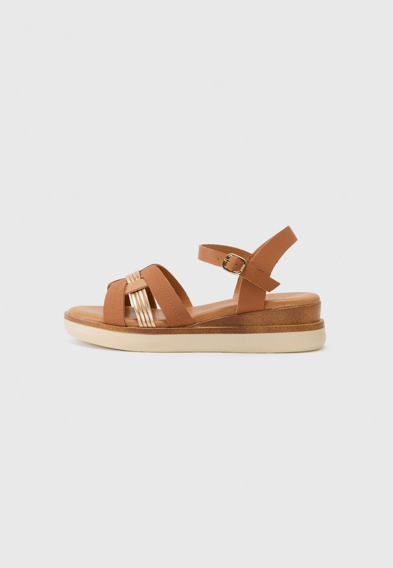 Sandal in pelle marrone con una piattaforma spessa, presenta tre cinghie incrociate e una cinghia alla caviglia con fibbia, suola testurizzata e suola di colore chiaro.