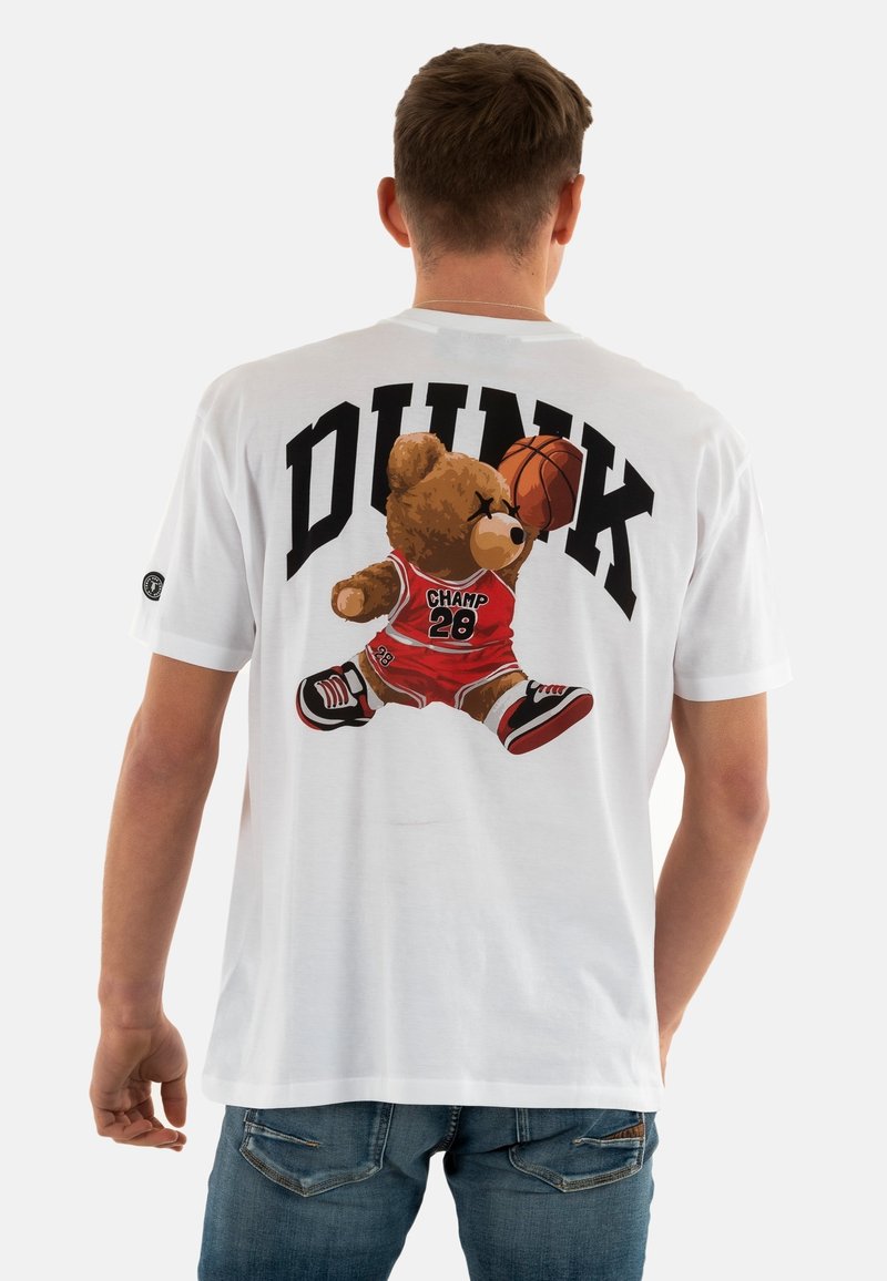 Camiseta de algodón blanca con un gráfico de un oso vestido con ropa de baloncesto roja y zapatos negros, con el texto "DUNK" arriba en negro.