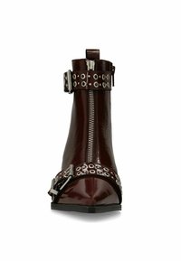 Bordeaux enkellaars met een glanzende afwerking, spitse neus, zijrits en gestudeerde riemaccenten met zilverkleurige hardware. Ontwerp met een platte zool.