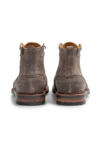 Bottines en daim marron avec une finition lisse, un bout arrondi et un talon en bois empilé, dotées de languettes sur le côté pour un enfilage facile.