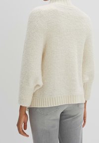 Kermanvärinen neulepaita, jossa on teksturoidun pehmeä, pörröinen pinta, pitkät hihat sekä resorinen poolokaulus ja helma. Yhdistetty vaaleanharmaisiin farkkuihin.