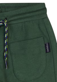 Des joggings en coton vert présentent une finition texturée, une taille élastique avec un cordon multicolore, et une poche plaquée avec une étiquette de la marque.