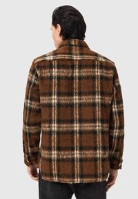 Brun ternet flannel-skjorte med en blød, tekstureret overflade. Har mørkegrønne og hvide linjer, en krave og knappede manchetter.