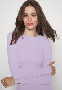 Dlhý rukáv fialový top vyrobený z elastického materiálu, s okrúhlym výstrihom a jemným logom Roxy na hrudi. Hladká textúra.