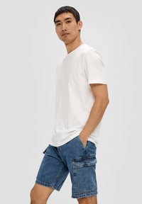 Witte T-shirt met korte mouwen gecombineerd met blauwe denim cargoshorts met twee zijzakken en een iets relaxte pasvorm.