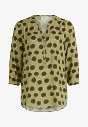 Blusa verde con escote en V, mangas largas, cierre de botones y un patrón de grandes círculos marrones contorneados en blanco. Textura de tela suave.