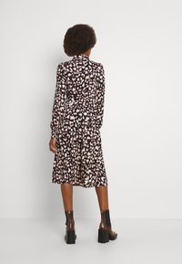 Vestido midi de manga larga con base negra, que presenta un estampado de leopardo en tonos rosa y crema. El vestido tiene una cintura ceñida y una falda fluida.