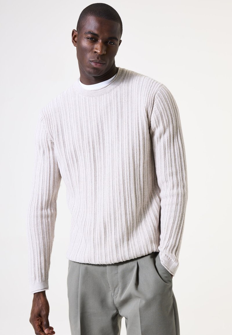 Suéter de punto acanalado gris claro con cuello redondo y mangas largas, combinado con pantalones sueltos de corte ligero en gris claro.