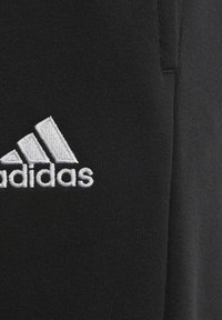 Närbild av svart tyg med vit broderad Adidas-logotyp som har tre ränder och text.