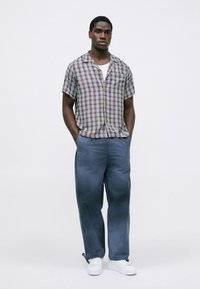 Kortermet rutete skjorte i rødt, blått og hvitt, kombinert med løstsittende blå bukser og hvite joggesko, som viser en avslappet passform og knappedetalj.