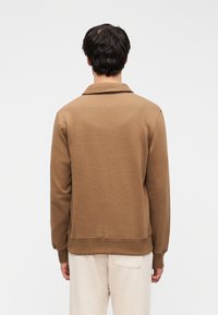 Καφέ βαμβακερό φούτερ με γιακά, μακριά μανίκια και άνετη εφαρμογή. Ομαλή υφή με ριμπ τελείωμα και μανσέτες.