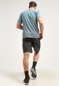 Camiseta deportiva en azul claro con un diseño texturizado, combinada con pantalones cortos oscuros. Calcetines atléticos negros y zapatillas completan el atuendo.