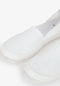 Scarpe bianche slip-on con un materiale superiore liscio e una suola in gomma con texture intrecciata, dal design minimalista e senza abbellimenti visibili.