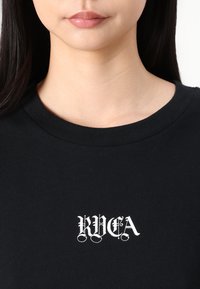 Juodas medvilninis marškinėliai su apvalia kaklo iškirpte ir trumpomis rankovėmis, priekyje su baltu stilizuotu tekstu "RVCA", glotni tekstūra.