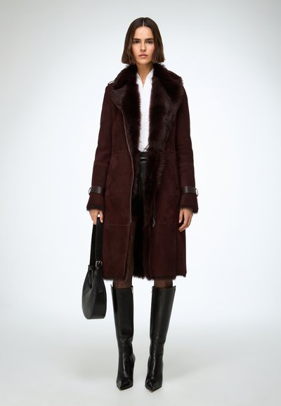 Kabát z bordového semišu s umelým kožúškom na golieri, so zipsovým zapínaním a dlhými rukávmi. Kombinovaný s čiernymi čižmami do kolien a čiernou kabelkou.