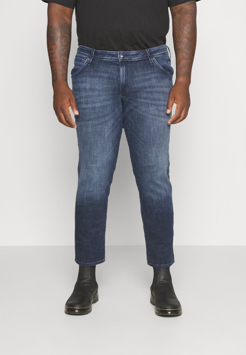 Mørkeblå denimjeans med slim fit, der har forlommer og knaplukning. Bæres med sorte ankelstøvler.