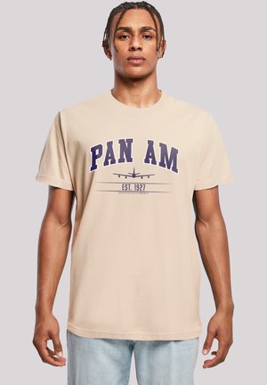 Beige Baumwoll-T-Shirt mit dem Schriftzug "PAN AM" in lila Fettdruck sowie einer Flugzeuggrafik und "EST. 1927" darunter. Lässig geschnitten.