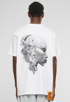 White cotton t-shirt featuring a large gray and white floral robotic face graphic on the back, with an orange label at the hem.