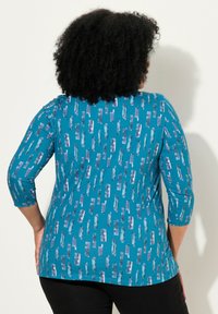 Teal, pitkähihaisen yläosan, jossa on pystysuuntainen siveltimenveto-kuvio eri sävyissä purppuraa. Valmistettu pehmeästä, joustavasta materiaalista, jossa on pyöreä kaula-aukko.