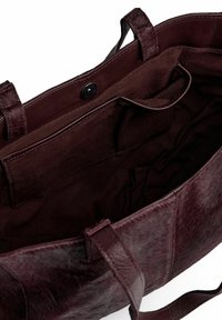 Burgundowa skórzana torba tote z teksturowaną powierzchnią, dwiema uchwytami, zapięciem na zatrzask i wewnętrzną kieszenią. Wykończona gładkim materiałem.