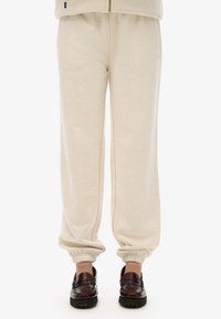 Pantaloni della tuta beige con cintura elastica e polsini, realizzati in morbido cotone, con vestibilità rilassata e tasche laterali.